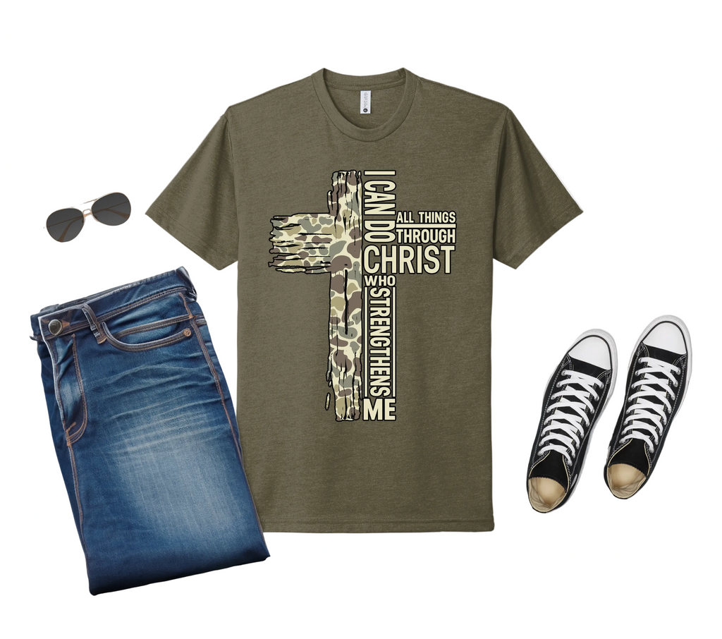 Military green t-shirt with cross design and text, paired with jeans and sneakers on a light gray background.